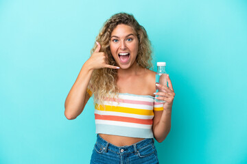 Young blonde woman with a bottle of water isolated on blue background making phone gesture. Call me back sign