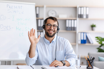 Glad middle aged european man in glasses and headphones waving hand to webcam