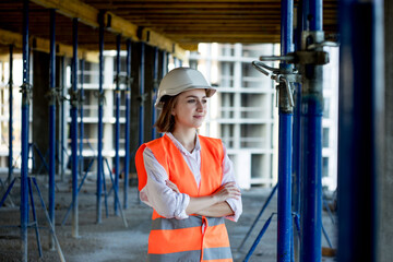 Portrait of beautiful female architect who stands idly and smiles against the background of buildings, outdoors