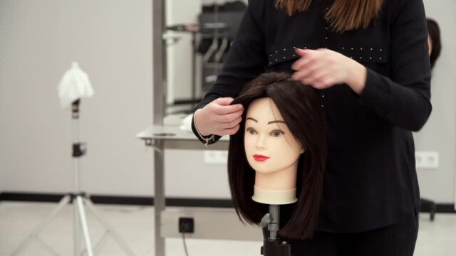 a girl in black clothes cuts the hair of a mannequin
