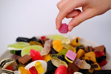 close-up of child's hand taking one gelatin candy, gummy bear, colored gelatinous sweets, black licorice candies, unhealthy food concept, halal gelatin, selective focus at shallow depth of field - obrazy, fototapety, plakaty