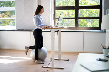 Woman Using Adjustable Height Standing Desk In Office