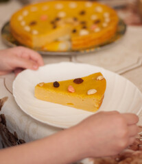 A piece of pumpkin pie with nuts on a white plate on a blurry background of hands