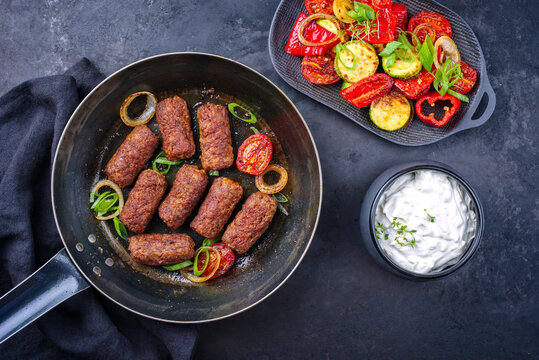 Traditional Croatian cevapi spicy meat ball rolls with BBQ vegetable and tzatziki served as top view in a skillet