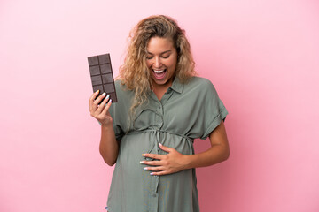 Girl with curly hair isolated on pink background pregnant and holding chocolate with surprised...