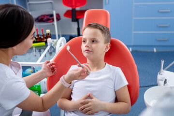female dentist talks to young boy and tells him how to take care of his teeth. handsome boy is smiling in dentist's office. concept is a children's medical examination.