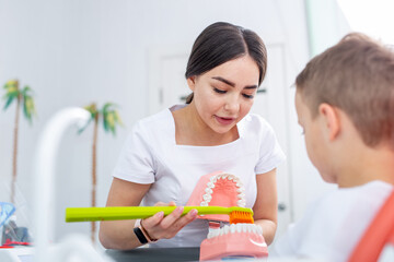 Obraz na płótnie Canvas female dentist shows a young boy how to brush his teeth properly. handsome boy is smiling in dentist's office. concept is a children's medical examination.