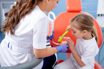 pediatric dentist shows how to properly brush a little girl's teeth. A beautiful girl is smiling in dentist's office. concept is a children's medical examination.