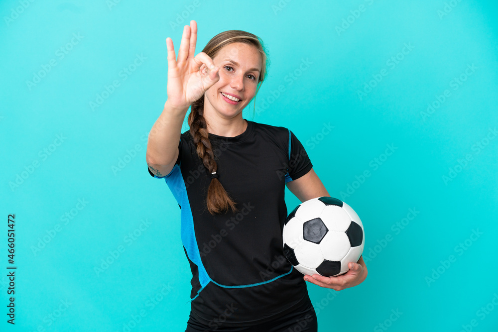 Wall mural Young English woman isolated on blue background with soccer ball and making OK sign