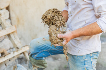 Worker applying mud plaster to a traditional stone house.
