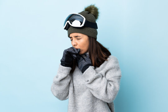 Mixed race skier girl with snowboarding glasses over isolated blue background coughing a lot.