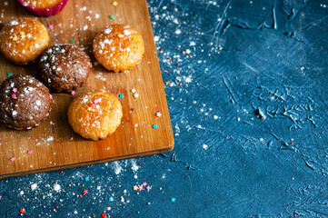 Цooden kitchen board  with fresh baked homemade muffins strewn with multicolored sugar decorations  on dark blue texture background.