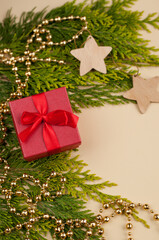 red gift box on the background of a thuja branch with a shiny golden garland and wooden decoration