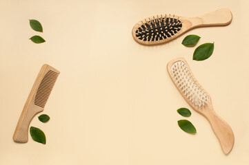 three different wooden combs on a beige background with green leaves with a place for text