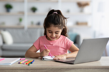 Little Girl Drawing In Notepad While Study Online With Laptop At Home