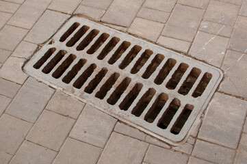 Metal storm grate on rectangular gray paving slabs