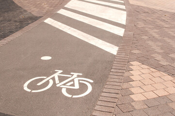 A sign drawn in white paint signifying a bicycle path on gray asphalt and a pedestrian crossing...