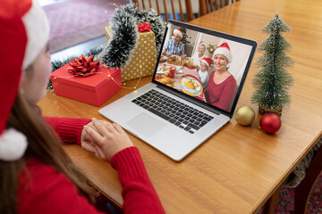 Naklejka na ściany i meble Caucasian woman in santa hat making christmas laptop video call with smiling family at dinner table