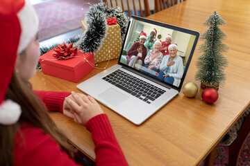 Obraz na płótnie Canvas Caucasian woman in santa hat making christmas laptop video call with smiling diverse senior friends