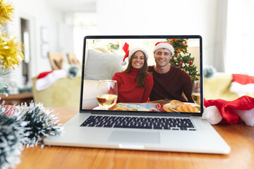 Smiling caucasian couple in christmas santa hats on laptop video call interface screen