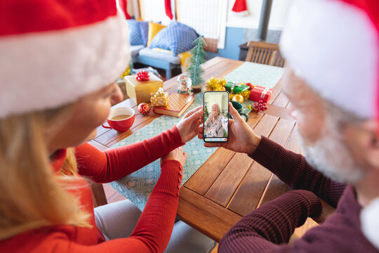 Caucasian couple in santa hats making christmas smartphone video call with happy senior woman