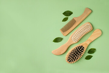 three massage wooden combs and several green leaves on a green background in a vertical arrangement with space for text
