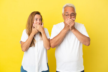 Middle age couple isolated on yellow background covering mouth with hands
