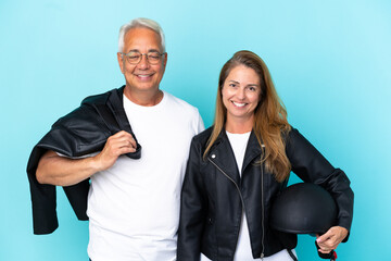 Middle age bikers couple with a motorcycle helmet isolated on blue background posing with arms at hip and smiling