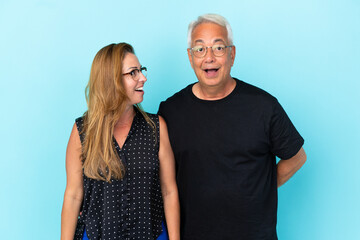 Fototapeta premium Middle age couple isolated on blue background with surprise facial expression