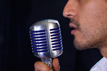 Curly-haired Mexican pop singer singing with a microphone against a black background