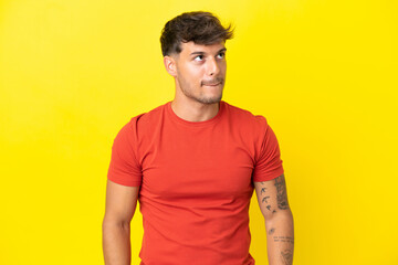 Fototapeta premium Young caucasian handsome man isolated on yellow background having doubts while looking up