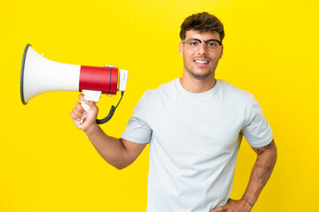 Young caucasian handsome man isolated on yellow background holding a megaphone and smiling