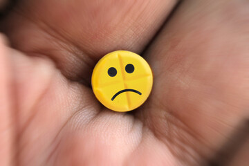 Pill with sad smiley logo in palm of the hand, close-up