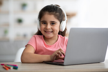 Cute Little Arab Girl Wearing Wireless Headphones Using Laptop At Home