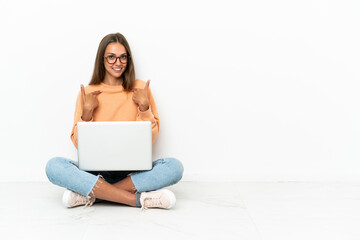 Young woman with a laptop sitting on the floor with surprise facial expression