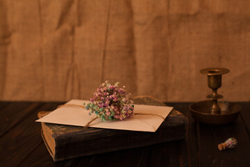 vintage still life, in historical style, a gift letter with a bouquet of dried flowers tied with twine, lies on an old book and next to a retro candlestick with a small flask