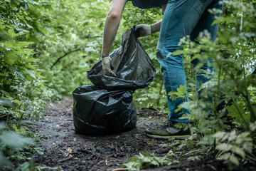 volunteer cleaner is cleaning up park and standing by bunch of garbage bag