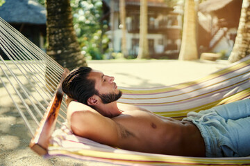 Tropical vacation. Young man relaxing on hammock in beach resort.