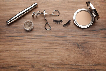 Flat lay composition with eyelash curler, makeup products and accessories on wooden table. Space for text