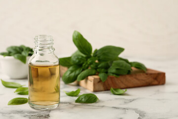 Glass bottle of basil essential oil and leaves on white marble table. Space for text