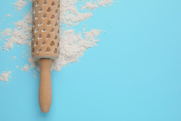 Wooden rolling pin and flour on light blue background, top view. Space for text