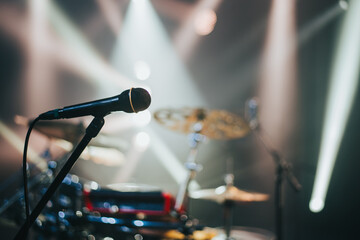 Close shot of a microphone standing on a stage with a drum kit in the background