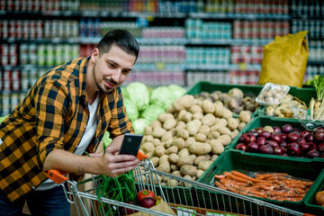 Young handsome man in a supermarket using smartphone while grocery shopping