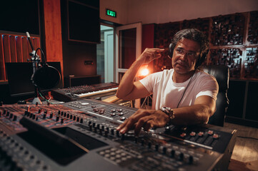 Senior hispanic music producer working on a mixing soundboard while in his studio