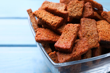 Crispy rye rusks in bowl on light blue wooden table, closeup