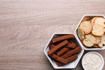 Different crispy rusks and dip sauce on wooden table, flat lay. Space for text