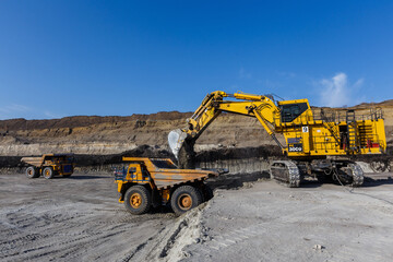 Industrial work in an open pit coal mine. Close-up. A large excavator pours soil into a large yellow dump truck.