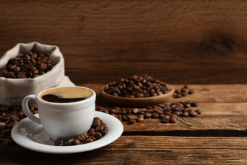 Cup of aromatic hot coffee and beans on wooden table, space for text