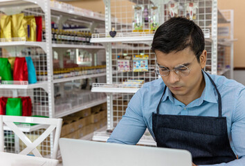 Young male owner uses computer and software to check stocks and goods in his startup bakery or café shop. Smart male shop owner uses technology to improve his online business and increase his sales