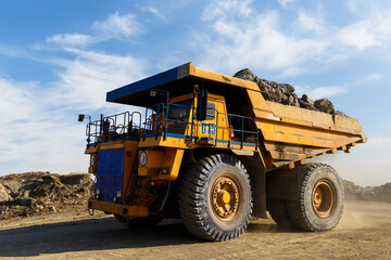 Industrial work in an open pit coal mine. A large yellow dump truck is carrying coal soil through the quarry. Open pit coal mining.